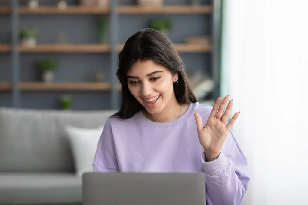 Woman waving during an online therapy video session from home